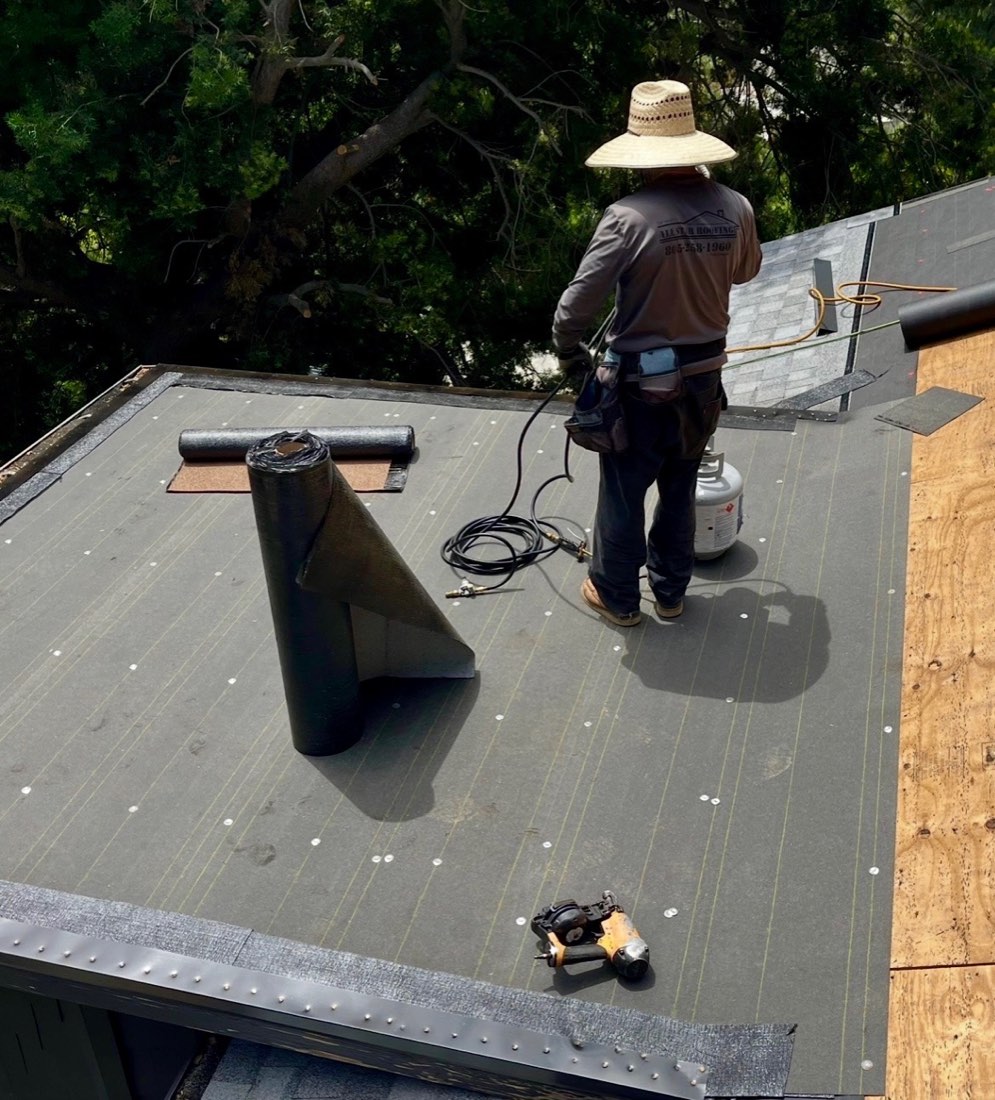An All Star Roofing crew member laying torch-down underlayment on a flat roof section during a re-roof